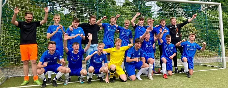 Eine Fußballmannschaft in blauen Trikots jubelt vor einem Tor auf einem Spielfeld.