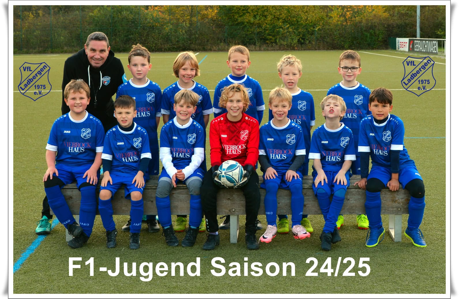 Eine Fußballmannschaft, junge Spieler in blauen Trikots, lächelnd; ein Trainer steht daneben.